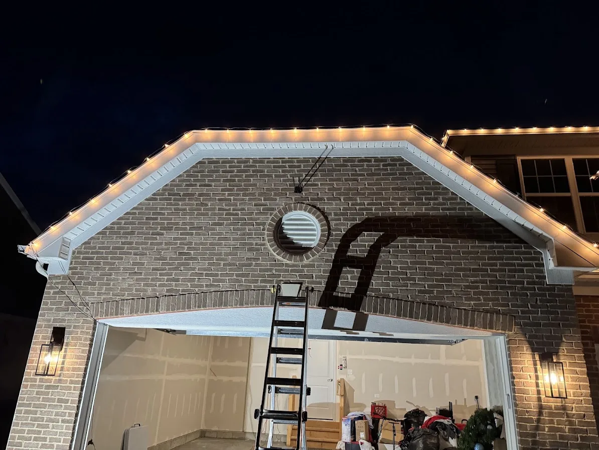 Brick garage at night with warm white holiday lights along the gable