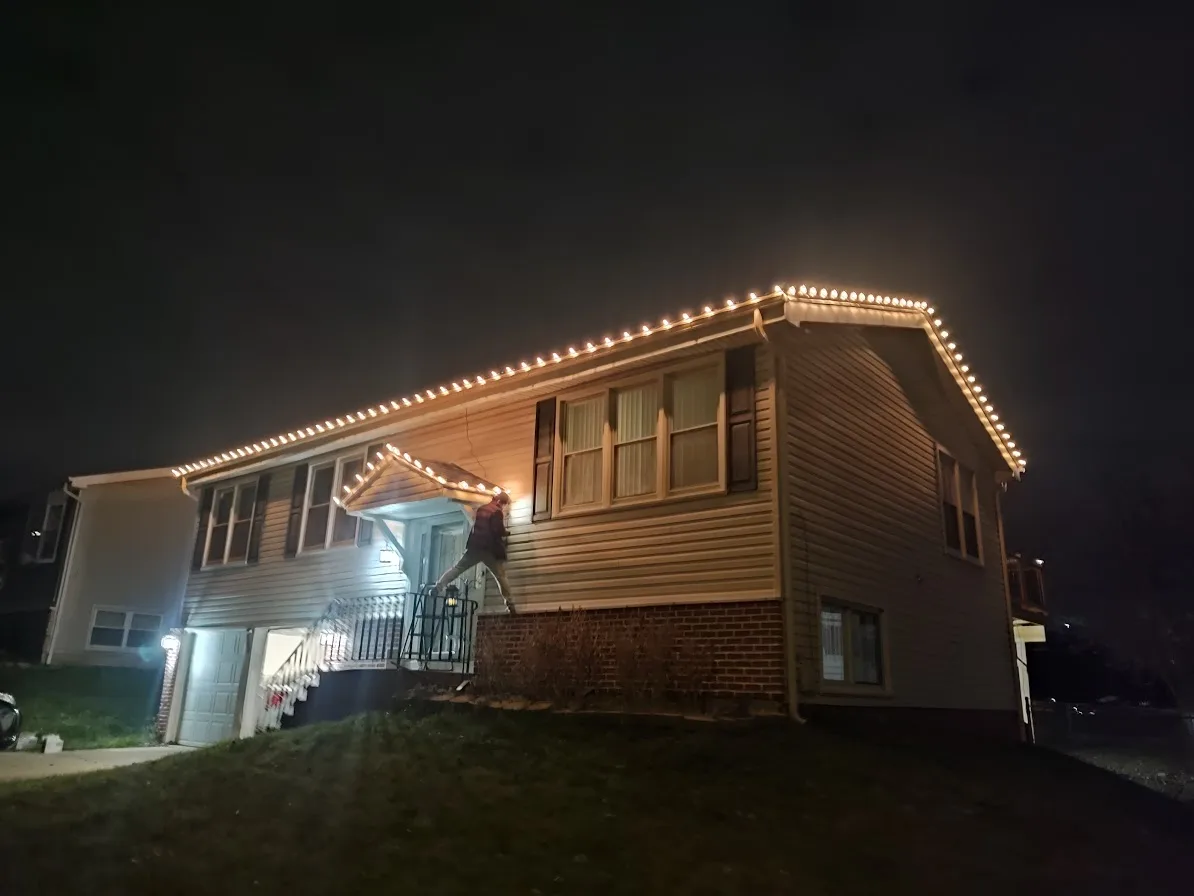 Wide nighttime view of a home with warm white holiday lights tracing the roofline