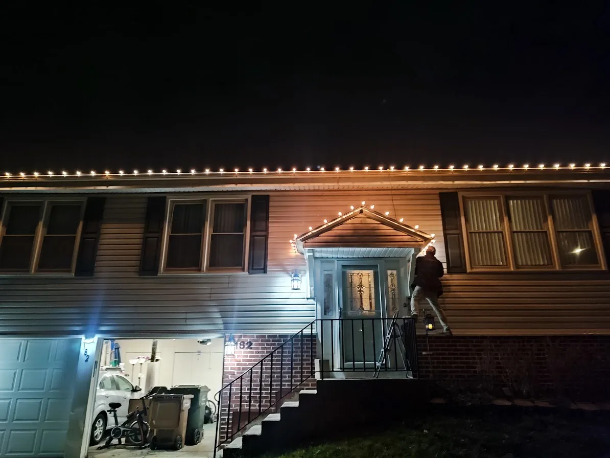 Front nighttime view of warm white holiday lights across a home and entry gable