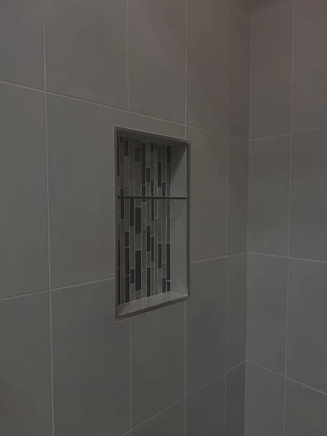 Close view of a tiled shower niche with mosaic accent