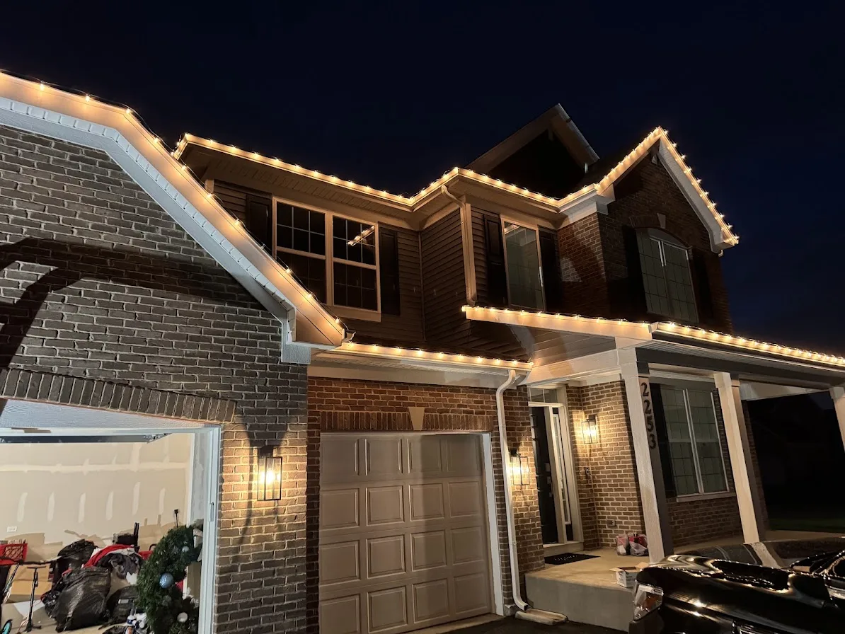 Brick home at night with warm white holiday string lights outlining the roof